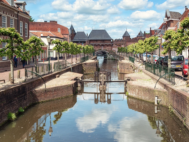 Koppelpoort Amersfoort surrounded by a bridge over water, with green trees and a blue sky.