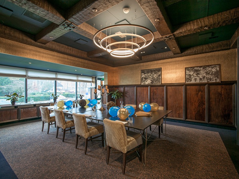 Meeting room in Amrâth Berghotel Amersfoort with a large wooden table with blue and gold balloons on it, beige chairs with plenty of daylight.