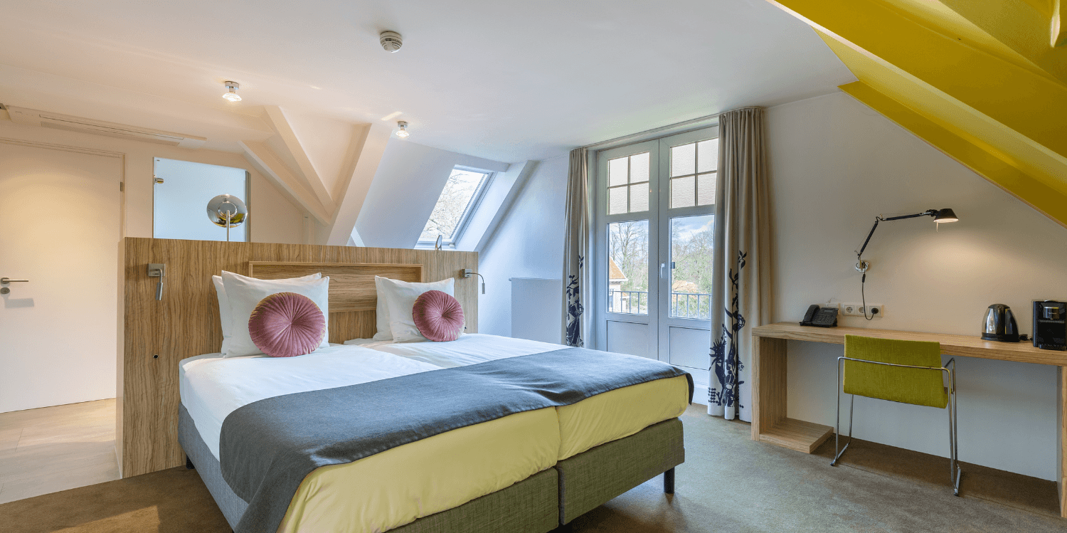 Superior tweepersoonskamer in Amrâth Berghotel Amersfoort met twee eenpersoonsbedden, een houten scheidingswand, een bureau met gele accenten en een opvallende gele muur onder een schuin dak.