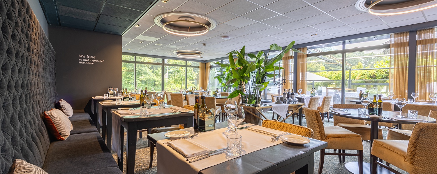 Eine High Tea im Amrâth Berghotel Amersfoort auf einem runden Tisch gedeckt mit einem weißen Tischtuch, darauf eine Etagere mit herzhaften und süßen Häppchen, daneben Geschirr, eine Teekanne, zwei Weingläser.