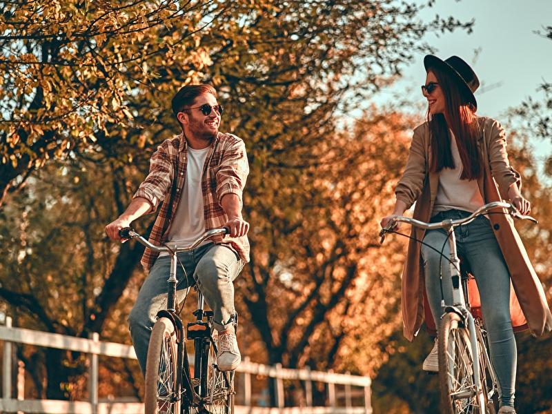 Mann und Frau fahren lachend nebeneinander an einem sonnigen Herbsttag Fahrrad.