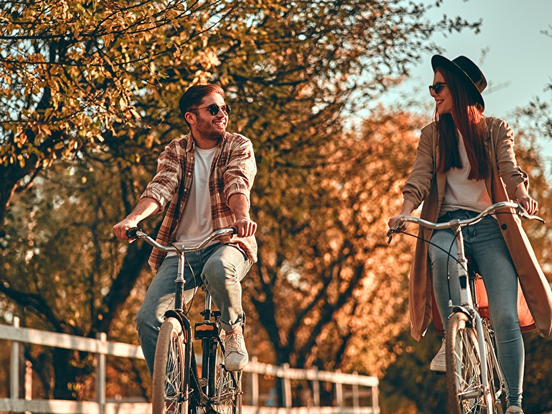Man en vrouw fietsen lachend naast elkaar op een zonnige herfstdag.