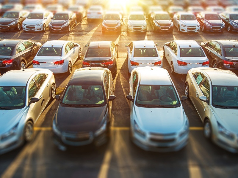 A parking lot with multiple rows of parked cars with the setting sun in the background
