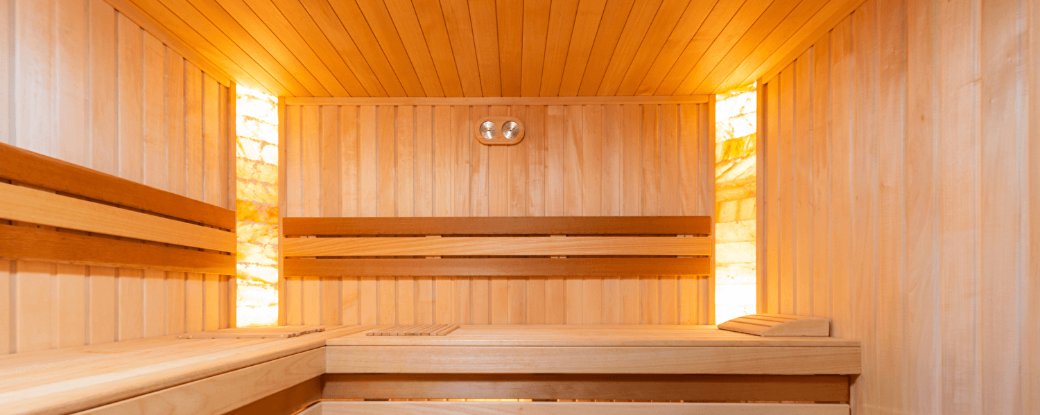 Innenraum einer traditionellen Holzsauna mit warmer Beleuchtung und mehreren Sitzebenen für optimale Entspannung.